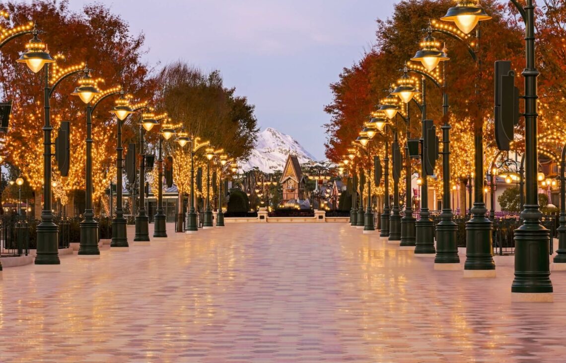 Vue sur l'entrée monumentale d'Adventure Way à Disney Adventure World, une promenade arborée style Belle Époque menant vers le lac.