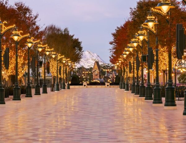 Vue sur l'entrée monumentale d'Adventure Way à Disney Adventure World, une promenade arborée style Belle Époque menant vers le lac.