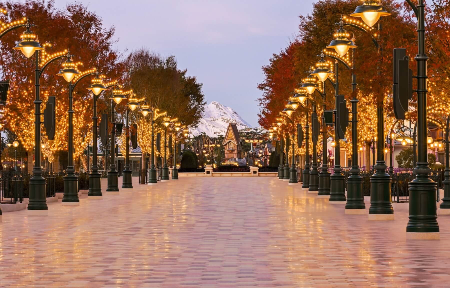 Vue sur l'entrée monumentale d'Adventure Way à Disney Adventure World, une promenade arborée style Belle Époque menant vers le lac.